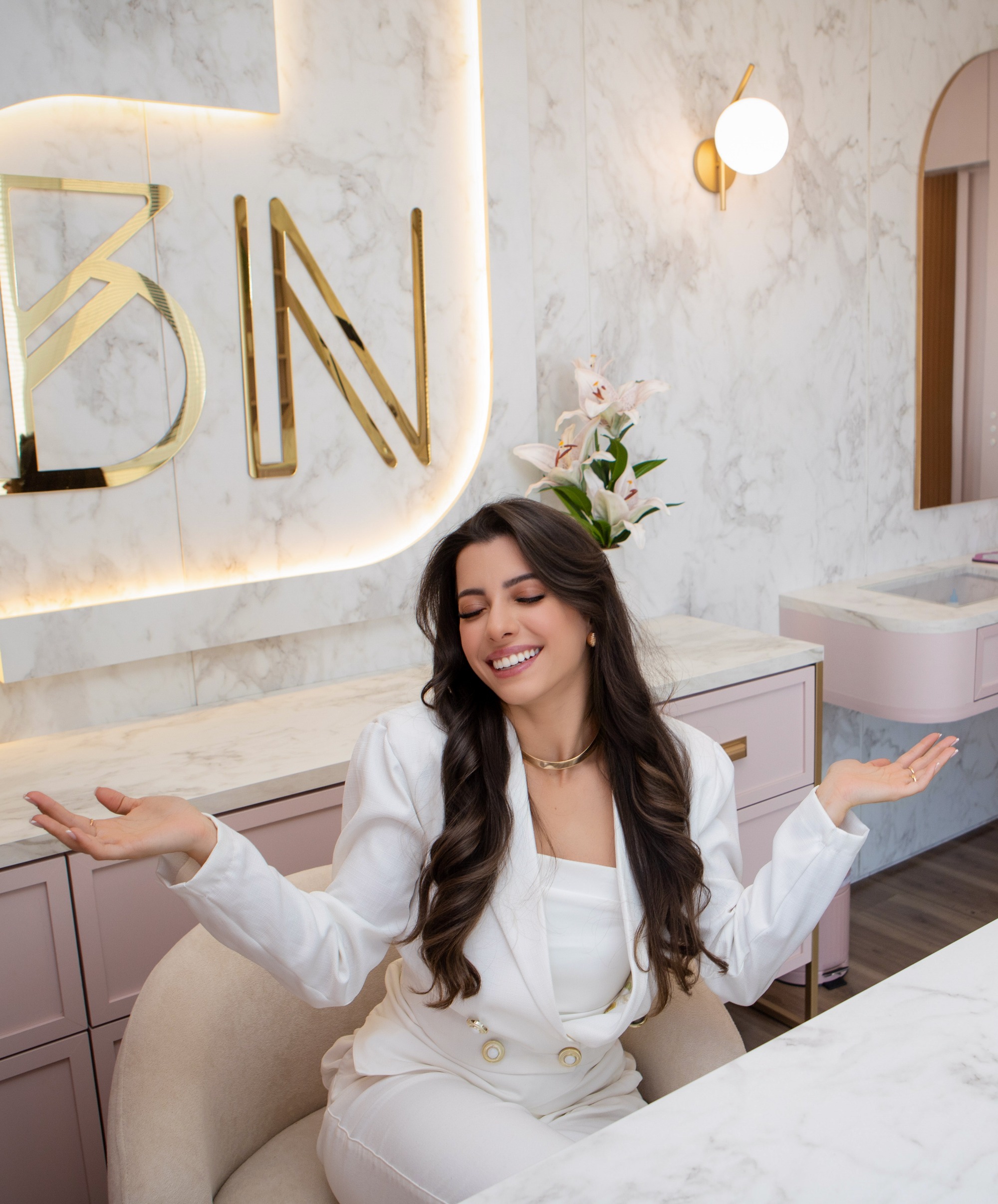 Bruna Nycole sorrindo na sala da BN Clinic, com o letreiro BN dourado ao fundo