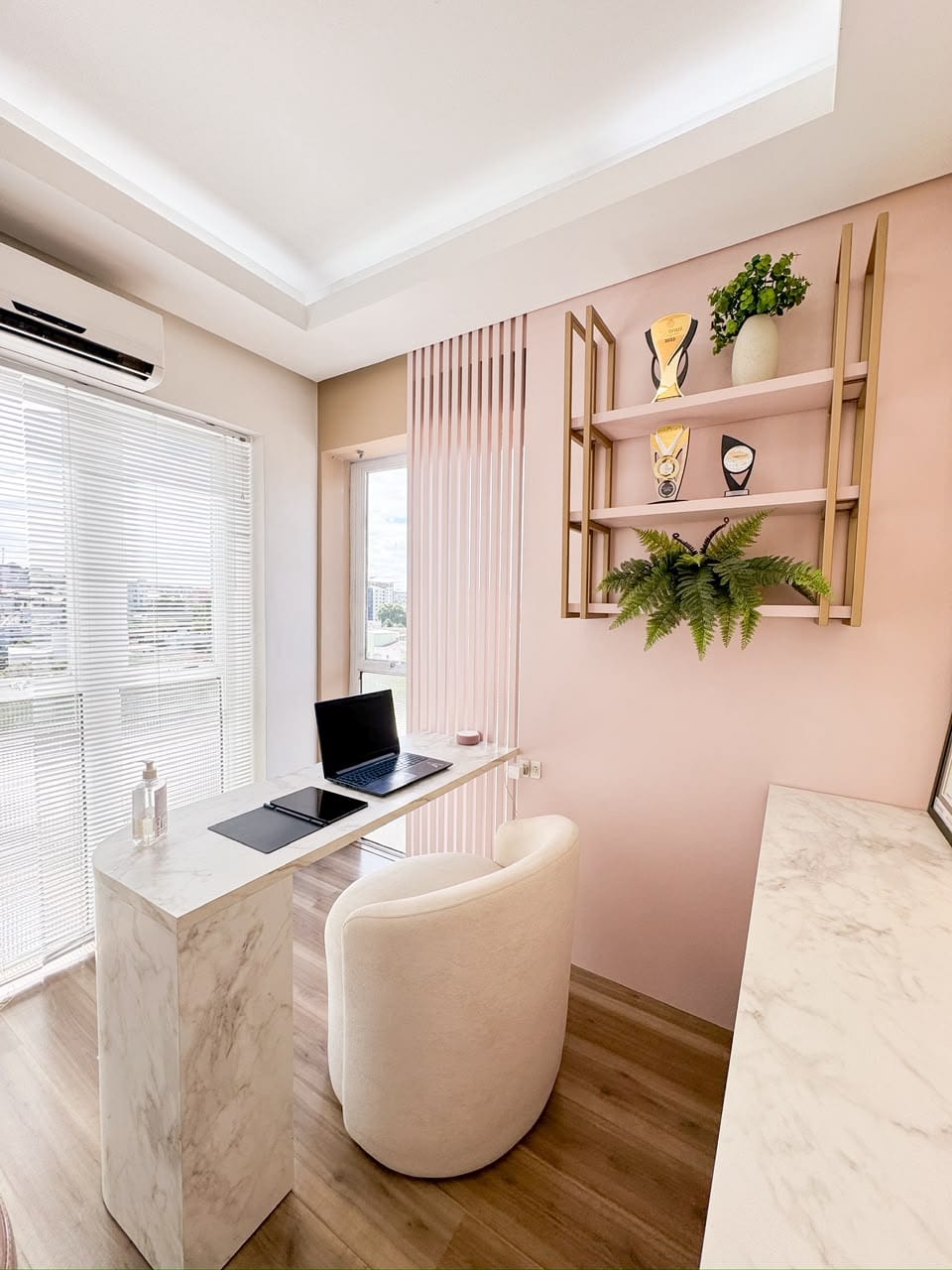 Sala da clínica com parede blush, prateleiras douradas e bancada de mármore
